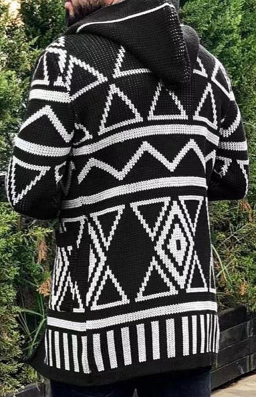 Back view of a person wearing a black and white long jacquard knitwear cardigan sweater with geometric patterns and a hood, standing outdoors.