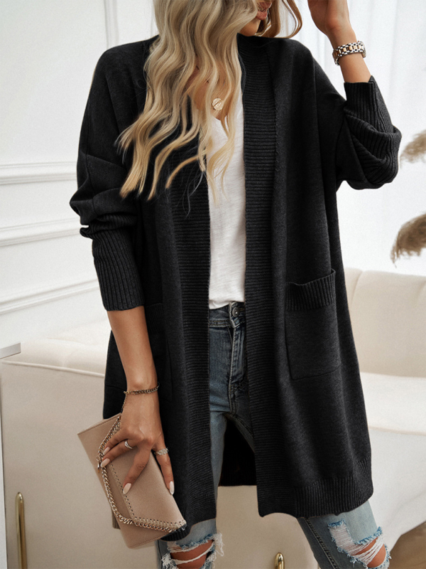 Woman wearing a black batwing sleeve cardigan solid color sweater jacket over a white top, paired with ripped jeans and holding a clutch purse.