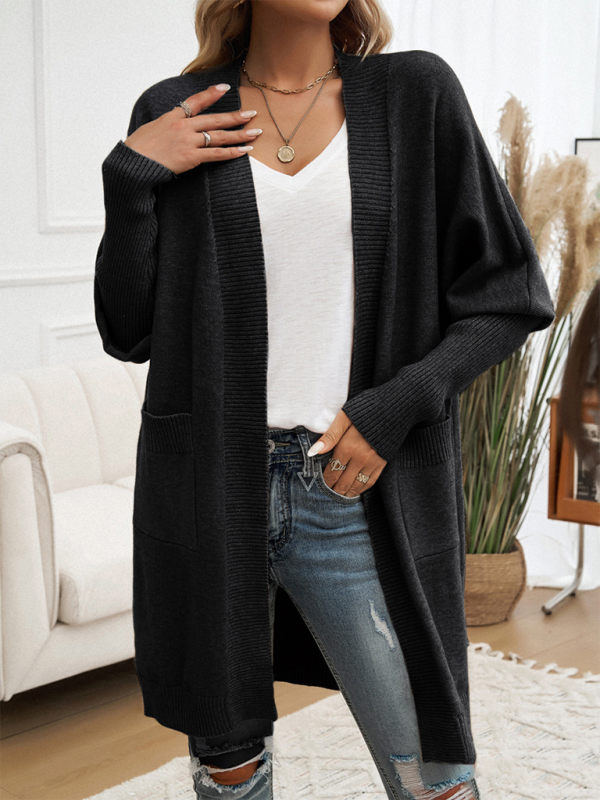 Woman wearing a black batwing sleeve cardigan sweater jacket over a white top and distressed jeans in a stylish indoor setting.