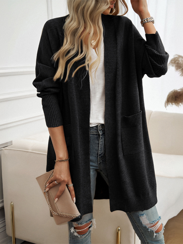 Woman wearing a black batwing sleeve cardigan solid color sweater jacket paired with a white top, ripped jeans, and holding a beige clutch.