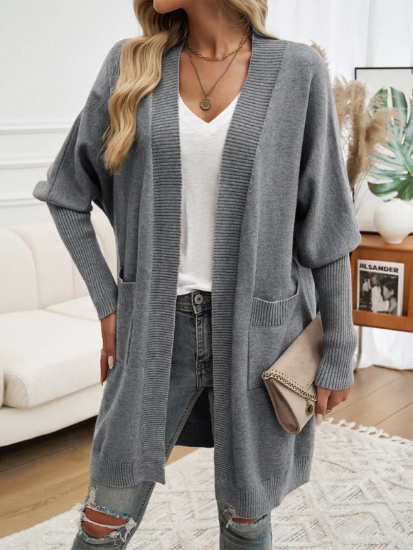 Gray Batwing Sleeve Cardigan Solid Color Sweater Jacket worn over a white V-neck T-shirt with distressed jeans, accessorized with a necklace and carrying a beige clutch inside a cozy living room setting.