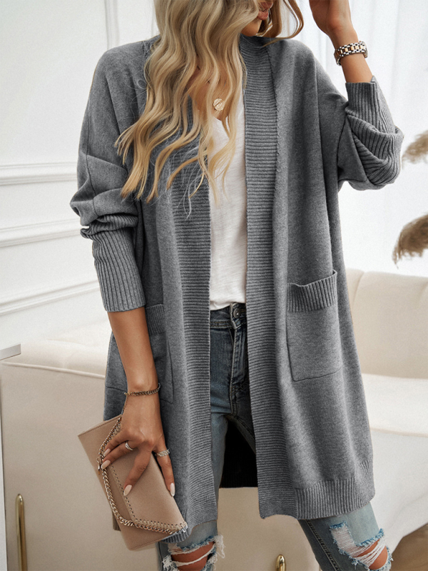 Woman wearing a gray batwing sleeve cardigan solid color sweater jacket with a white shirt, ripped jeans, and holding a beige clutch handbag.