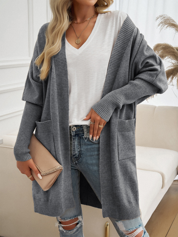 Woman wearing a gray batwing sleeve cardigan solid color sweater jacket over a white V-neck t-shirt, accessorized with a beige clutch purse and showcasing a casual autumn-winter look.